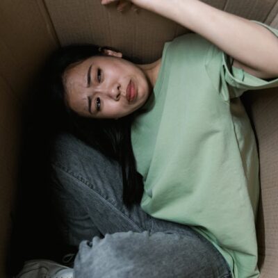 Woman enclosed in a cardboard box, showing signs of stress and fear.