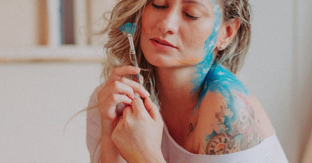 An artistic portrait of a woman with face and body paint holding a brush, eyes closed.