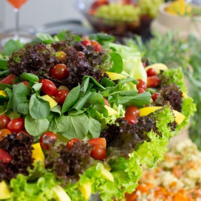 Colorful mixed salad with leafy greens, cherry tomatoes, and mango slices on a buffet table.