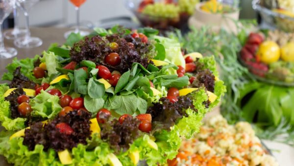 Colorful mixed salad with leafy greens, cherry tomatoes, and mango slices on a buffet table.