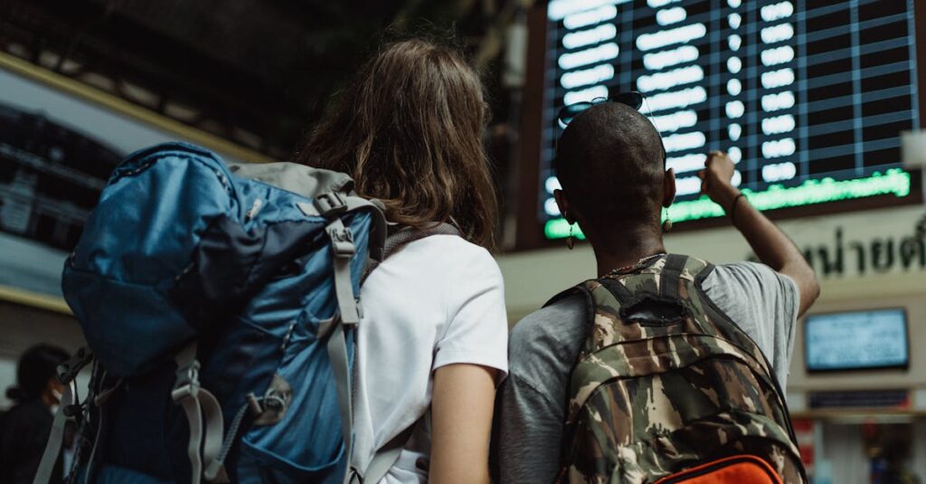 Two backpackers checking the digital board at a train station for travel information.