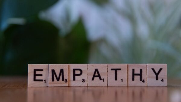 Close-up of tiles spelling empathy on a wooden surface with blurred green background.
