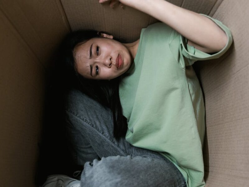 Woman enclosed in a cardboard box, showing signs of stress and fear.
