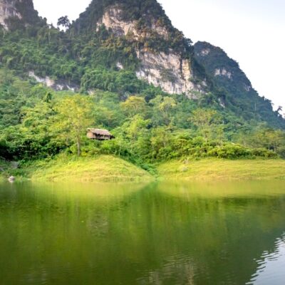 Amazing landscape of calm Na Hang lake surrounded by huge rocky mountains covered with green trees on sunny day in Tuyen Quang province