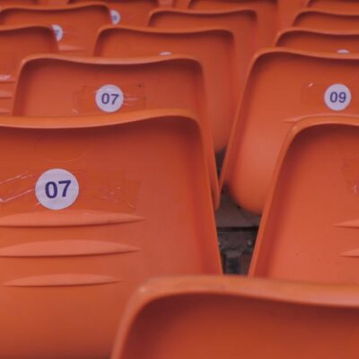 Rows of empty orange plastic stadium seats with visible numbered labels