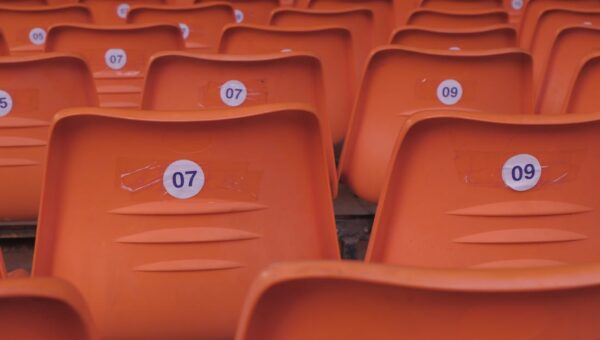 Rows of empty orange plastic stadium seats with visible numbered labels