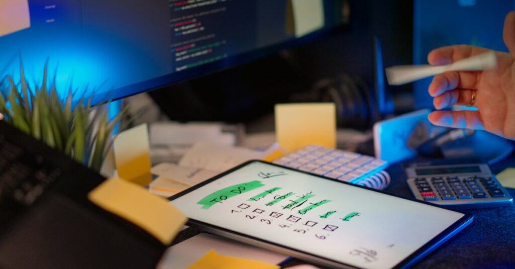 A cluttered desk with a tablet showing a to-do list, monitor showing code, and office supplies.