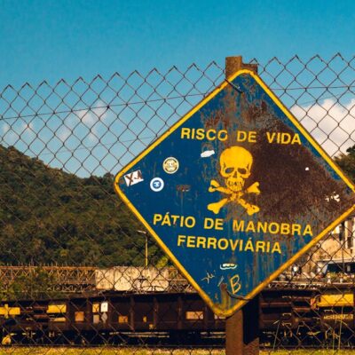 Rusty danger sign at a railway yard in São Paulo, Brazil under a bright blue sky.