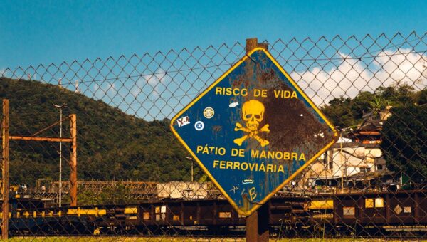 Rusty danger sign at a railway yard in São Paulo, Brazil under a bright blue sky.