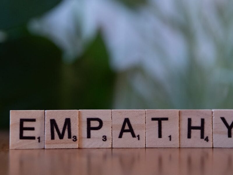 Close-up of tiles spelling empathy on a wooden surface with blurred green background.