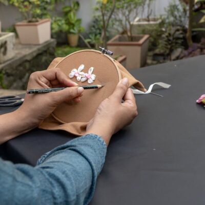 Hands embroidering outdoors with ribbons and yarns, showcasing arts and crafts.