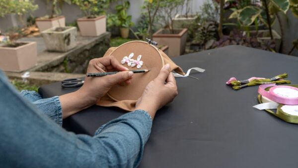 Hands embroidering outdoors with ribbons and yarns, showcasing arts and crafts.