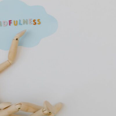 Wooden mannequin with mindfulness text on light blue cloud background, conveying calm.