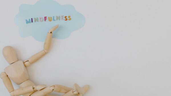 Wooden mannequin with mindfulness text on light blue cloud background, conveying calm.