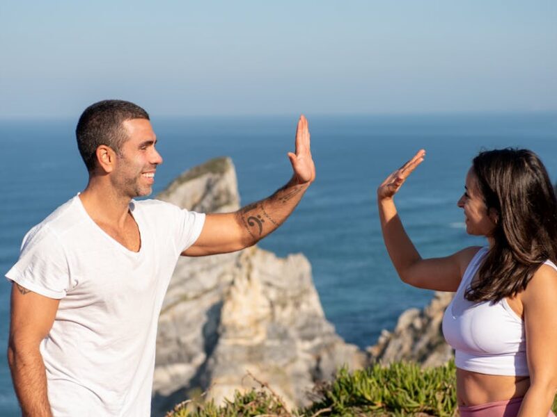 Fit couple in athletic wear high-fiving by the sea on a sunny day in Portugal.