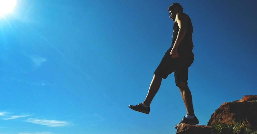 Man on a cliff's edge enjoying a bright sunny day outdoors.