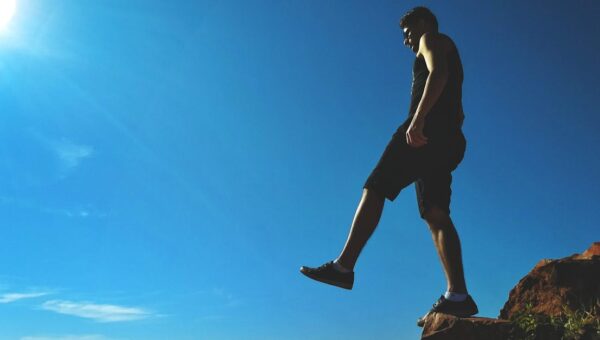 Man on a cliff's edge enjoying a bright sunny day outdoors.