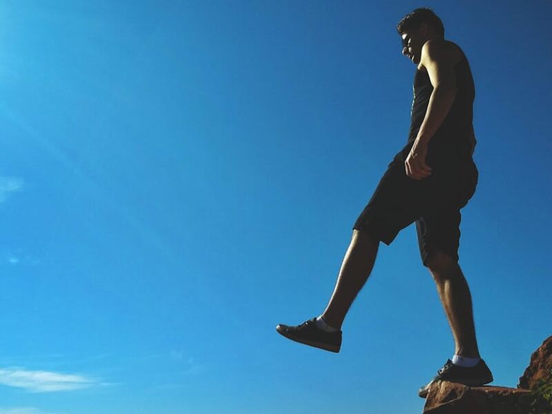 Man on a cliff's edge enjoying a bright sunny day outdoors.
