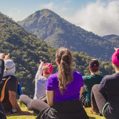 A diverse group of hikers enjoying a scenic mountain view while sitting on grass during the day.