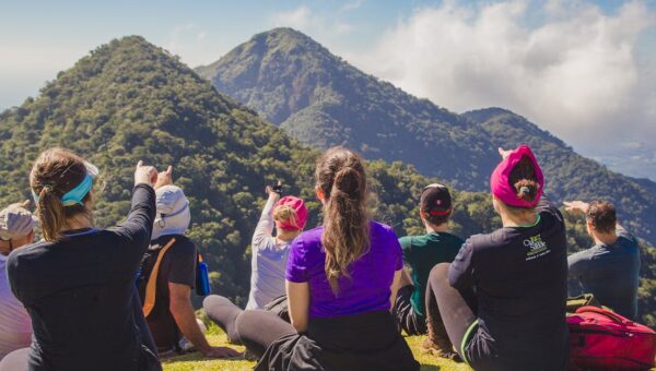 A diverse group of hikers enjoying a scenic mountain view while sitting on grass during the day.