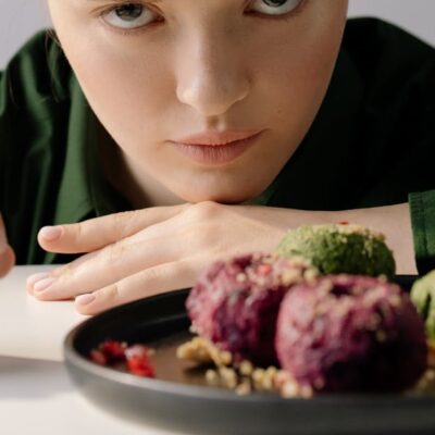 A woman intently observing traditional Georgian pkhali on a plate, showcasing beetroot and spinach varieties.