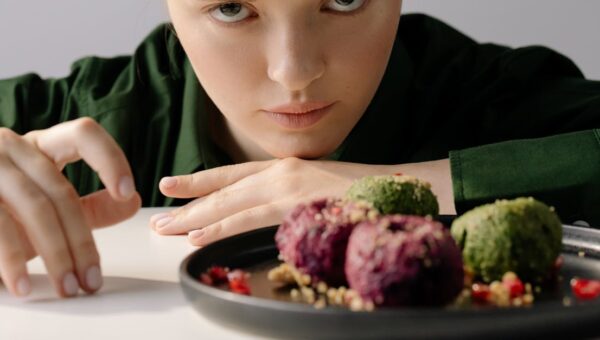 A woman intently observing traditional Georgian pkhali on a plate, showcasing beetroot and spinach varieties.