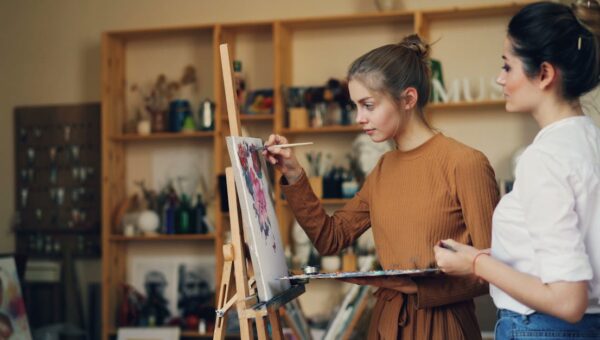 Two women engaged in creating art on canvas, showcasing creativity and concentration.
