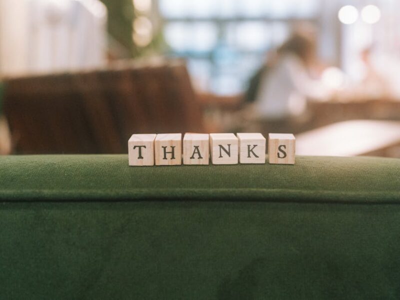 Wooden blocks spelling 'Thanks' on a green surface in relaxed indoor setting.