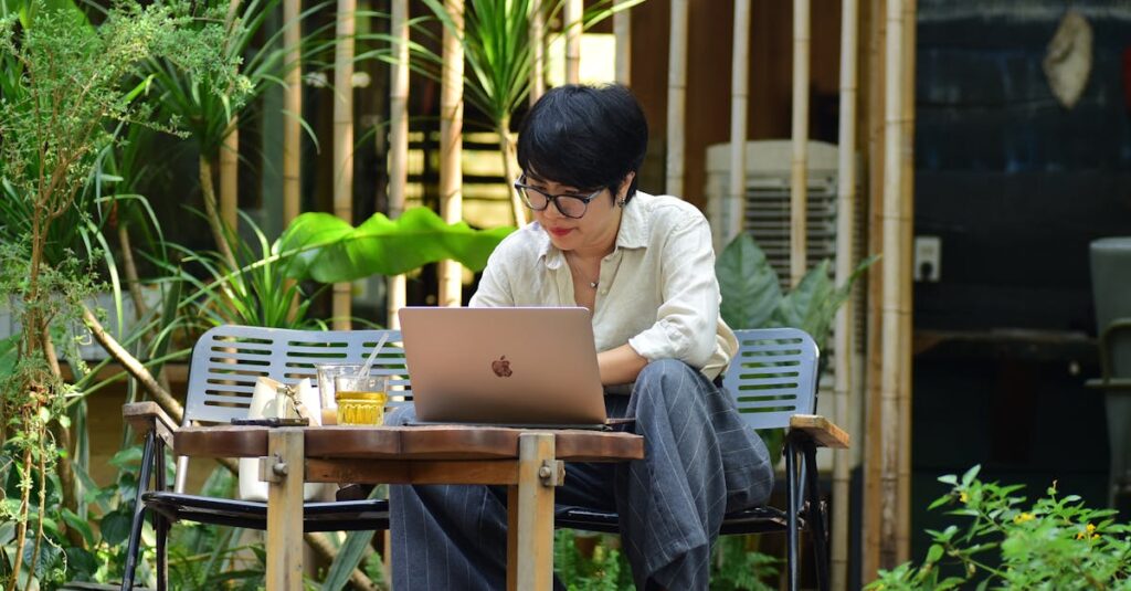 A woman focuses on her laptop while sitting in a lush outdoor cafe.