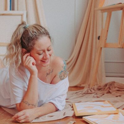 Smiling woman relaxing and creating art in a cozy room with canvases and paints.