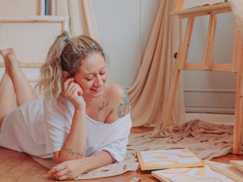 Smiling woman relaxing and creating art in a cozy room with canvases and paints.