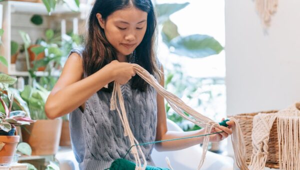 Asian woman skillfully crocheting with yarn in a comfortable indoor space surrounded by plants.