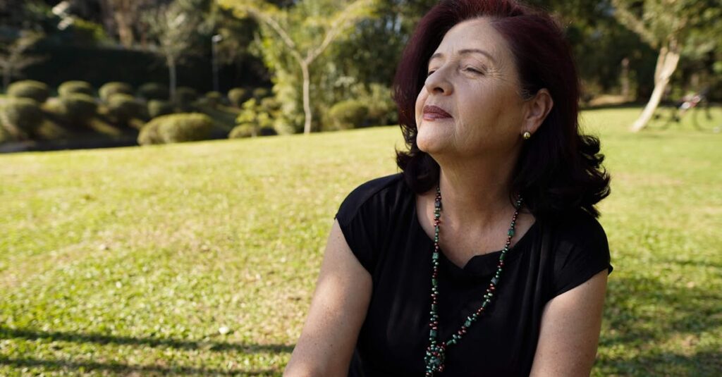 A relaxed, mature woman enjoys the sunlight in a tranquil park setting, exuding peace and contentment.