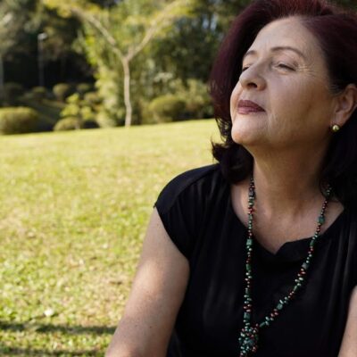 A relaxed, mature woman enjoys the sunlight in a tranquil park setting, exuding peace and contentment.