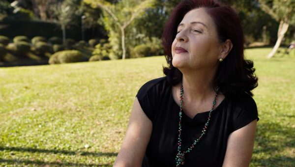 A relaxed, mature woman enjoys the sunlight in a tranquil park setting, exuding peace and contentment.