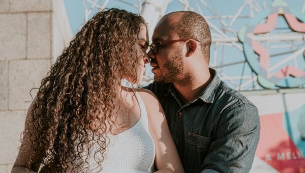 A romantic couple sharing a close moment outdoors in bright sunlight.