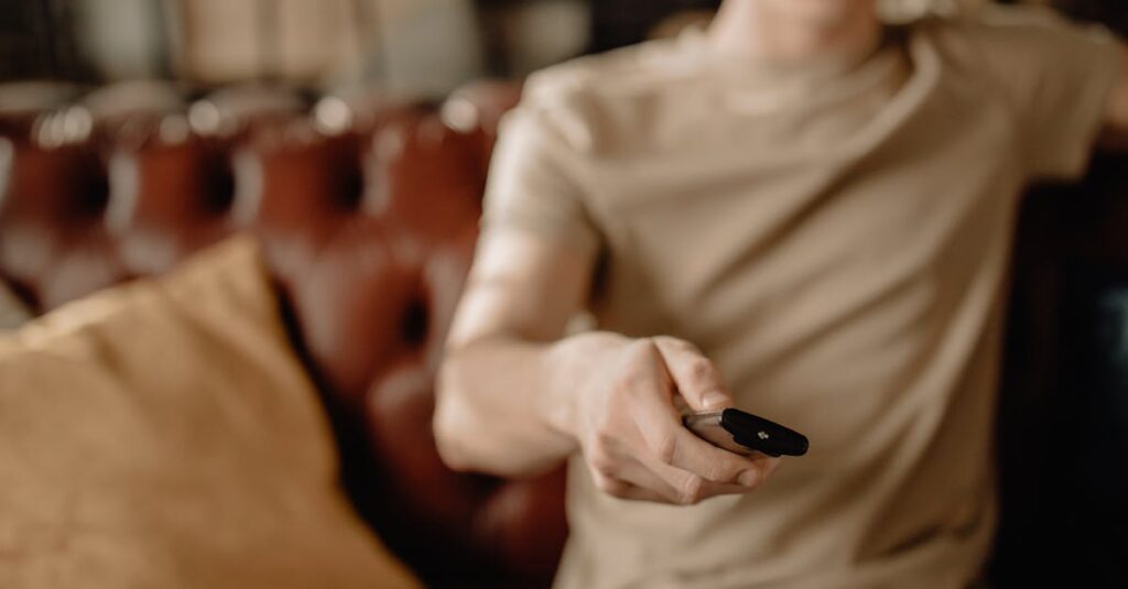 Person relaxing on a leather sofa at home, holding a remote control. Cozy and casual atmosphere.