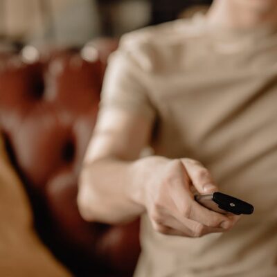 Person relaxing on a leather sofa at home, holding a remote control. Cozy and casual atmosphere.