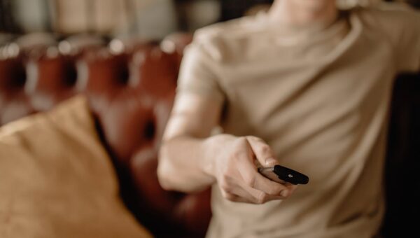 Person relaxing on a leather sofa at home, holding a remote control. Cozy and casual atmosphere.