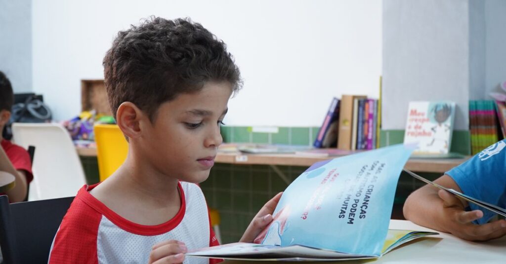 A young boy engrossed in reading a book in a classroom environment, promoting child literacy.