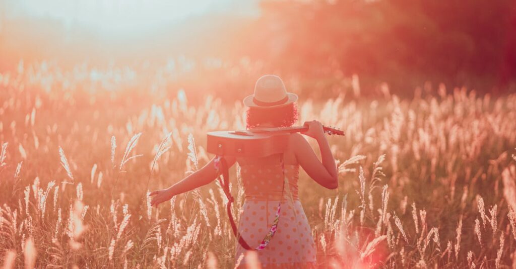 Woman in a field at sunset holding a guitar, embracing tranquility and freedom.