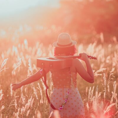 Woman in a field at sunset holding a guitar, embracing tranquility and freedom.
