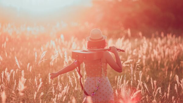 Woman in a field at sunset holding a guitar, embracing tranquility and freedom.