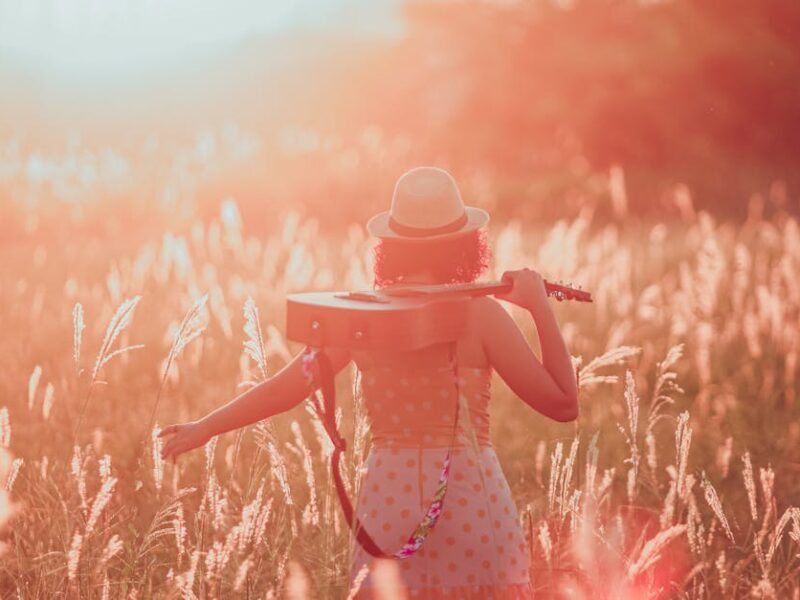 Woman in a field at sunset holding a guitar, embracing tranquility and freedom.