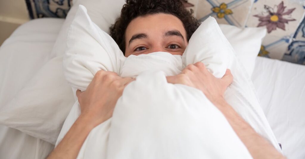 A young man relaxing in bed with a pillow, enjoying a peaceful morning indoors.