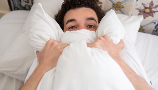A young man relaxing in bed with a pillow, enjoying a peaceful morning indoors.