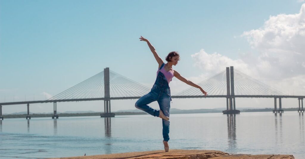 A woman performs a yoga pose on rocks near a scenic bridge over calm waters.
