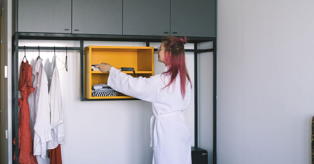 A woman in a bathrobe organizes a wardrobe in a modern hotel room.