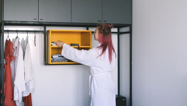 A woman in a bathrobe organizes a wardrobe in a modern hotel room.