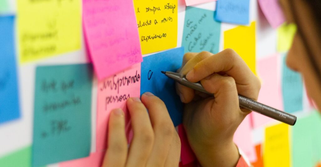 Como a Criatividade Pode Ajudar na Superação de Desafios Pessoais 2 Hands writing on colorful sticky notes during a brainstorming session indoors.